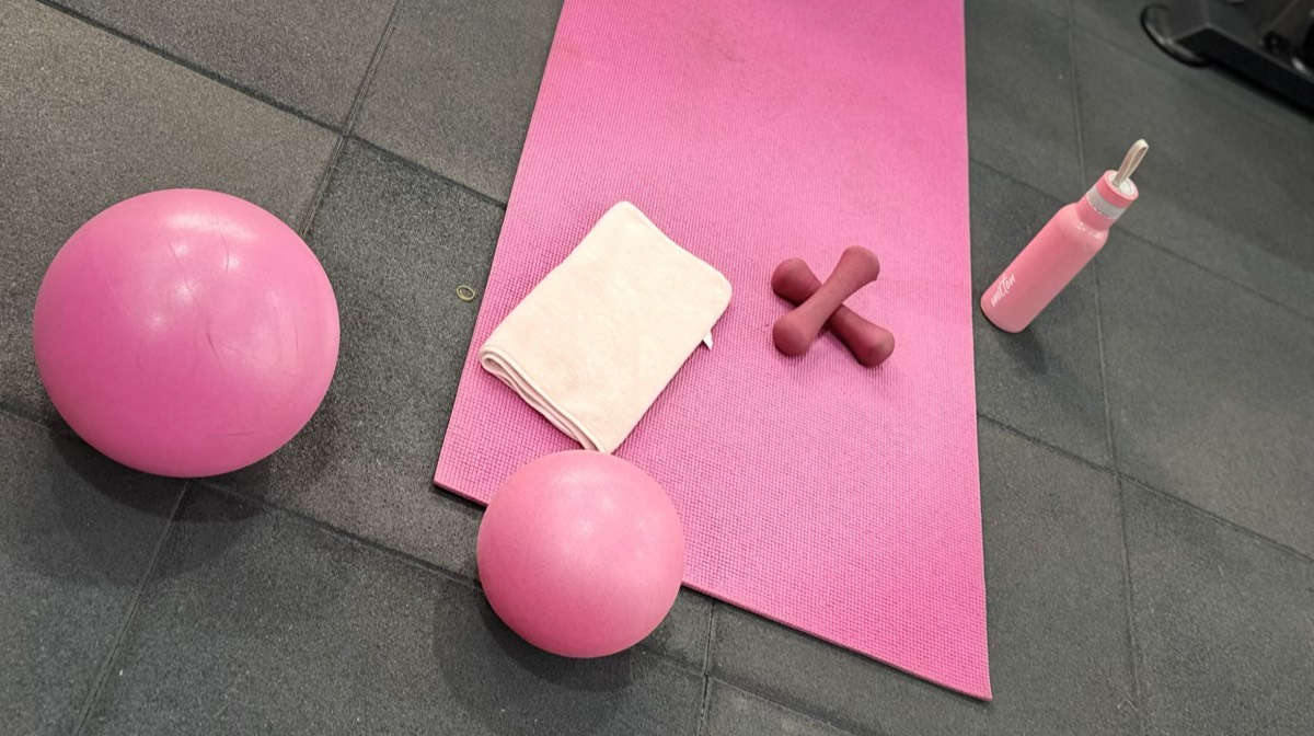 Soft pink stability balls, mat, light dumbbells, and towel laid out for gentle postpartum recovery movement